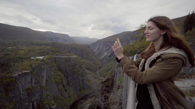 Young woman enjoy view and take photos at waterfall Voringfossen in Norway during fall / autumn