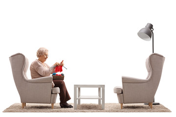 Lonely elderly woman sitting in an armchair and knitting