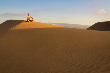 Obraz premium Man sitting and relaxing on sand dunes by the sunrise, in Maspalomas on Gran Canaria.