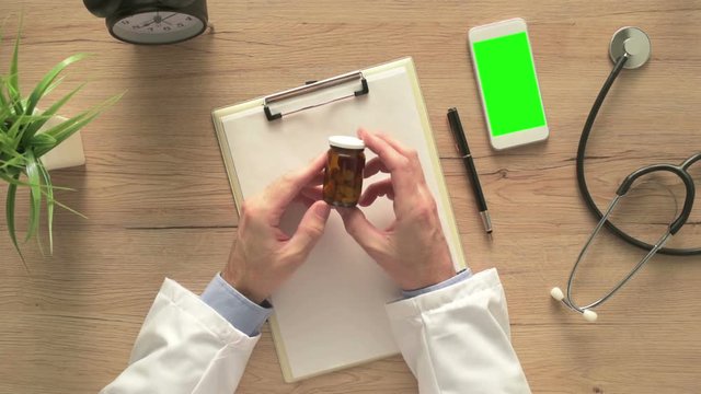 Overhead view of hospital office desk with male doctor holding unlabeled bottle of various pills and medication, generic drugs concept, prescription medicine and healthcare