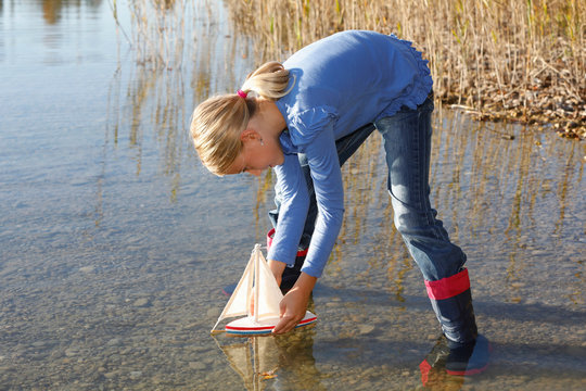 Young Girl Floating Toy Boat On Water