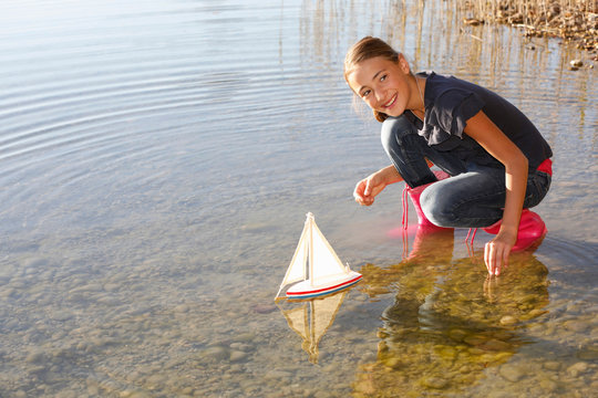 Young girl floating toy boat on water