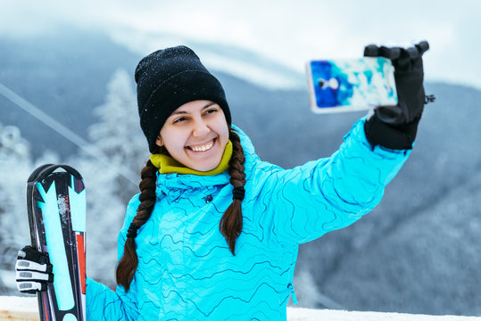 woman stands with ski  on the top of the hill and makes selfie