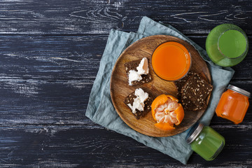 Breakfast, kiwi juice, carrot juice, crackers and cheese are served on a wooden plate. View from above.