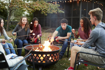 Teenage friends sit round a fire pit toasting marshmallows