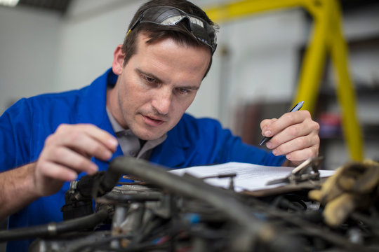 Male car mechanic with clip board checking car engine in repair garage