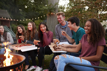 Teenagers at a fire pit eating take-away pizzas, close up - Powered by Adobe