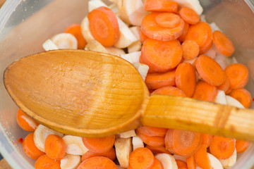 Natural wooden spoon in a bowl full of chopped vegetables - slices of carrot, pasternak and onions. Preparing soup for dinner. Healthy eating