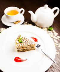 a piece of Esterhazy cake with nuts and apricot jam, with a cup of tea on white plate