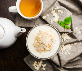 Delicate curd dessert Blancmange with almond flakes with a glass cup with a white kettle and a cup of tea