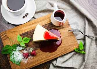 Italian dessert cheesecake with raspberry sauce and a cup of coffee on a wooden board