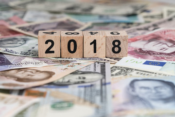 Year 2018 world economic or financial concept with cube wooden block number 2018 on pile of international mojor countries banknotes
