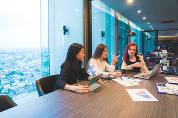Multi ethnic team of women discussing or having a brainstorm about startup plans or business ideas in modern office with city scape background.