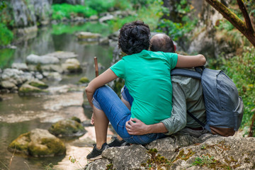Lovely adult couple hugging, sitting and relaxing by the river. Small mountain stream with moss covered rocks deep in the forest. Cliffs in Cheile Turzii, Romania. Autumn is coming. Calming nature