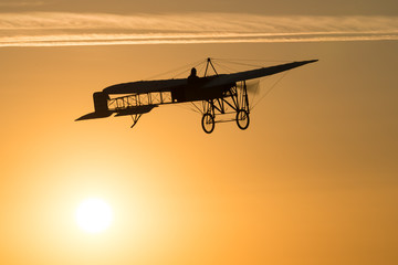 Old vintage airplane flying in an orange sky at sunset