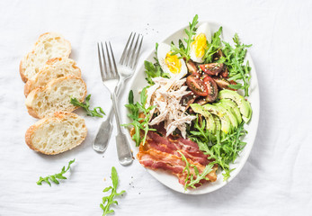 Boiled chicken, avocado, egg, arugula, tomato, bacon salad on a light background, top view
