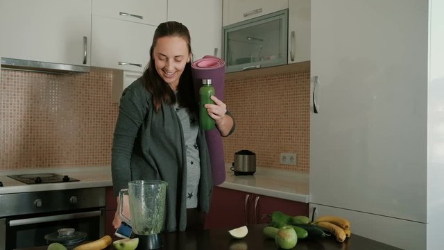 Young woman making a green vegetable smoothie on a blender and taking selfie photo with phone for social media and after eat chocolate
