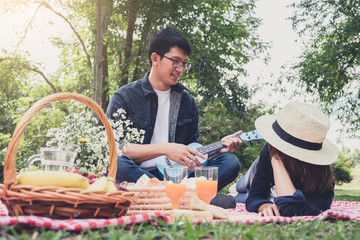 Naklejka na ściany i meble Happy Young man playing the guitar or Ukulele and Singing Song with couple love sitting on red classic picnic blanket, Love and tenderness, dating, romance