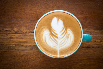 Cup of coffee on wooden table. Latte art in leaf shape. Top view with dark vignette. Warm color tone.