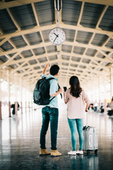 Asian couple traveler checking time with clock at train station during vacation trip