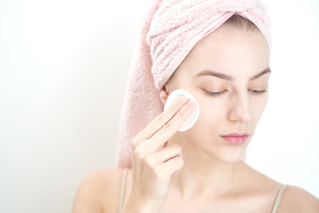 Facials. Girl with towel on head wipes clean the skin with a sponge on white background