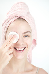 Facials. Girl with towel on head wipes clean the skin with a sponge on white background