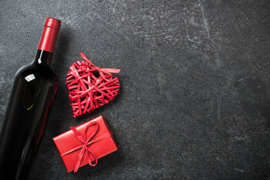Red wine bottle, gift box and wicker heart on black background