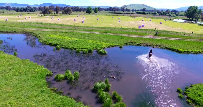 Aerial, horseback rider speeds through pond in Australia