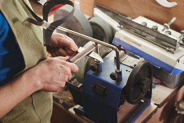 Making of a knife. Master sharpens a blade on the machine closeup in the Studio