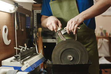 Making of a knife. Master sharpens a blade on the machine closeup in the Studio