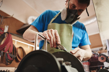 Making of a knife. Master sharpens a blade on the machine closeup in the Studio