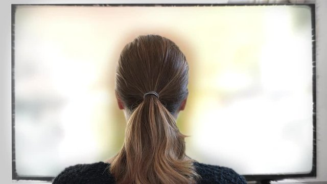 Watching Television Closely, Brainwash TV Concept. Young woman watching big screen television at home. Shot behind model shoulders.