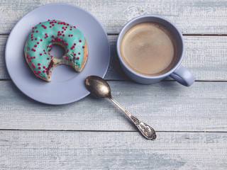 Donut with colorful icing and cup of coffee on a wooden background. Top view