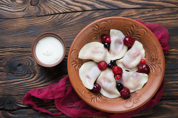 Boiled russian vareniki or dumplings with cherries and sour cream, top view on a rustic wooden...