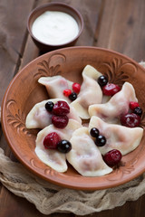 Boiled vareniki with cherry stuffing served in a clay plate, selective focus, vertical shot, close-up