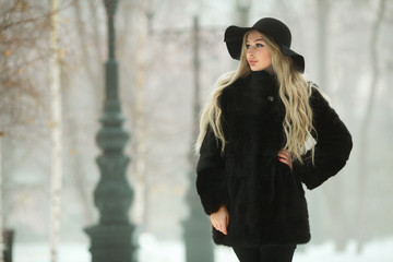 beautiful young girl in fur coat and hat walking in snow park