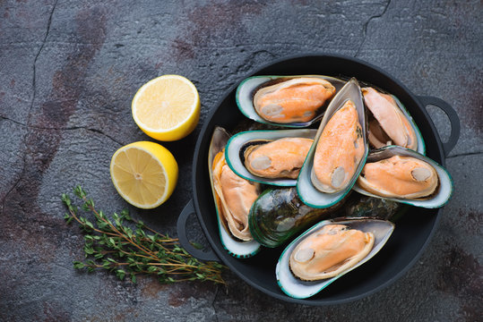 Cast-iron pan with fresh uncooked green mussels, thyme and lemon over cracked asphalt background. Horizontal shot with space, top view