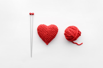 a knitted heart of red thread with an inserted knitting needle on a white background. and a hank of a red knitting thread
