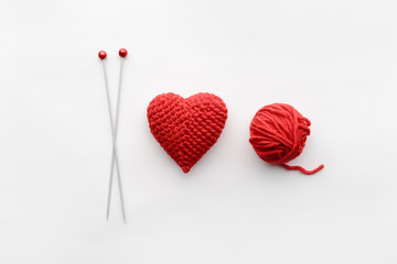 a knitted heart of red thread with an inserted knitting needle on a white background. and a hank of...