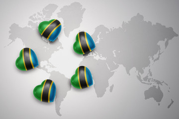 five hearts with national flag of tanzania on a world map background.