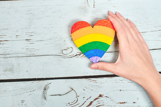 LGBT concept. Hand on wooden background holding heart rainbow colors