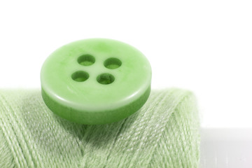 The needle, green button and the light green sewing reel. Conceptual photography of tailor's work.