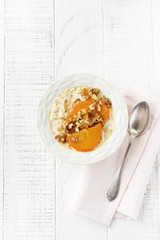 Oatmeal porridge with caramelized persimmon and walnuts in a light ceramic bowl on a white wooden background. Selective focus. Top view. Copy space.