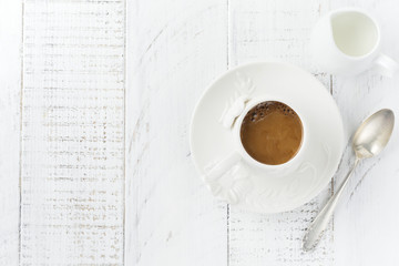 One white ceramic cup with coffee on a light wooden background. Selective focus. Top view. Copy space.