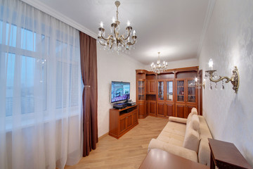 An office with a big window, dark curtains, a light sofa and the TV on a wall