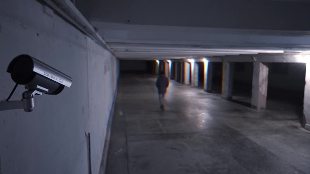 Kind of dangerous person walking at night on an underground passage in the background of a surveillance camera