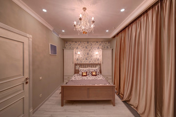 The bedroom with a bed and cream curtains, two cases and a beautiful crystal chandelier