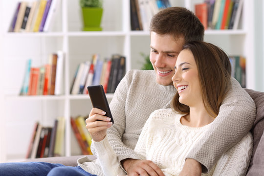 Couple watching media on a smart phone sitting at home