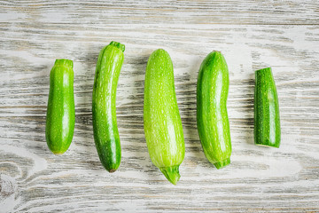 Fresh summer vegetables zucchini of different sizes on white shabby wooden background. Top view, space for text.