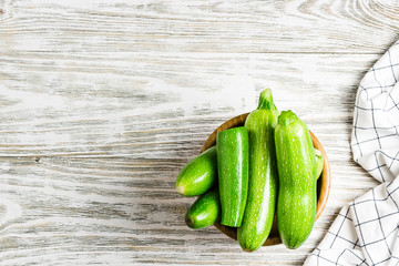 Fresh baby zucchini in a bowl on white shabby wooden background. Top view, space for text. 